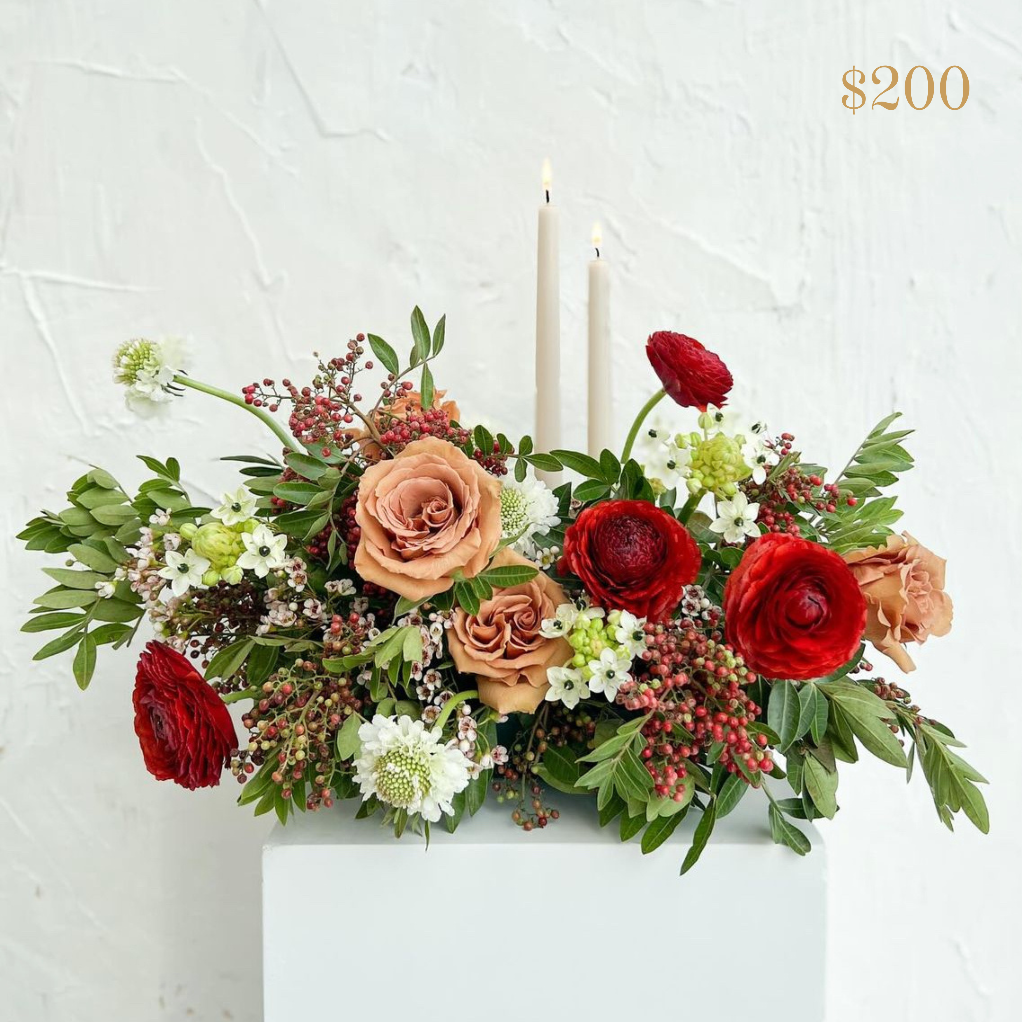 Red, white and toffee coloured flowers in a low centrepiece with 2 pillar candles. Text reading $200 value