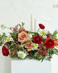 Red, white and toffee coloured flowers in a low centrepiece with 2 pillar candles. Text reading $200 value