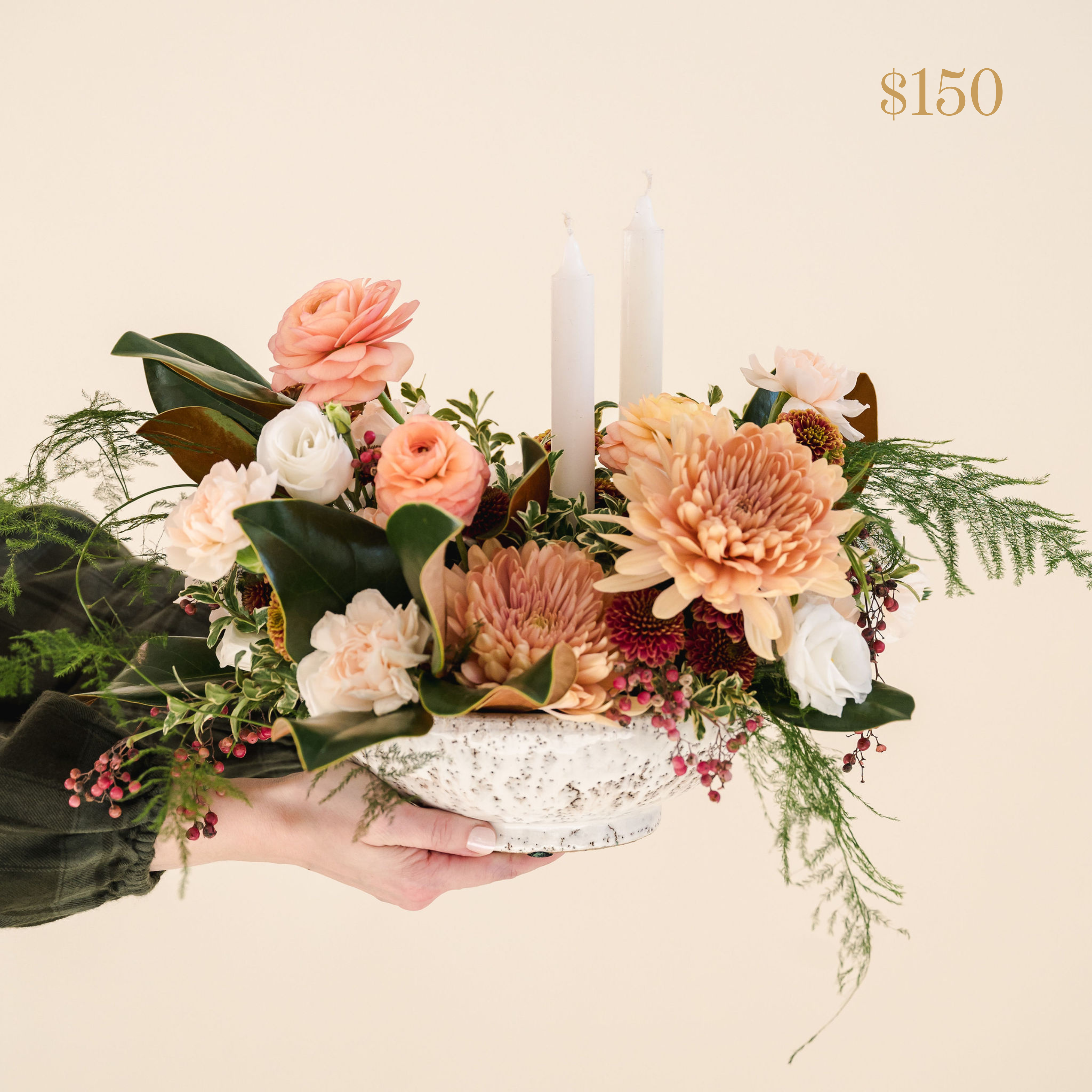 low lying centrepiece with a variety of greenery including peach, white and red flowers, two taper candles. Text reading $150 value