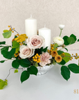 low centrepiece with two pillar candles, a variety of flowers and greenery. Text reading $150 value