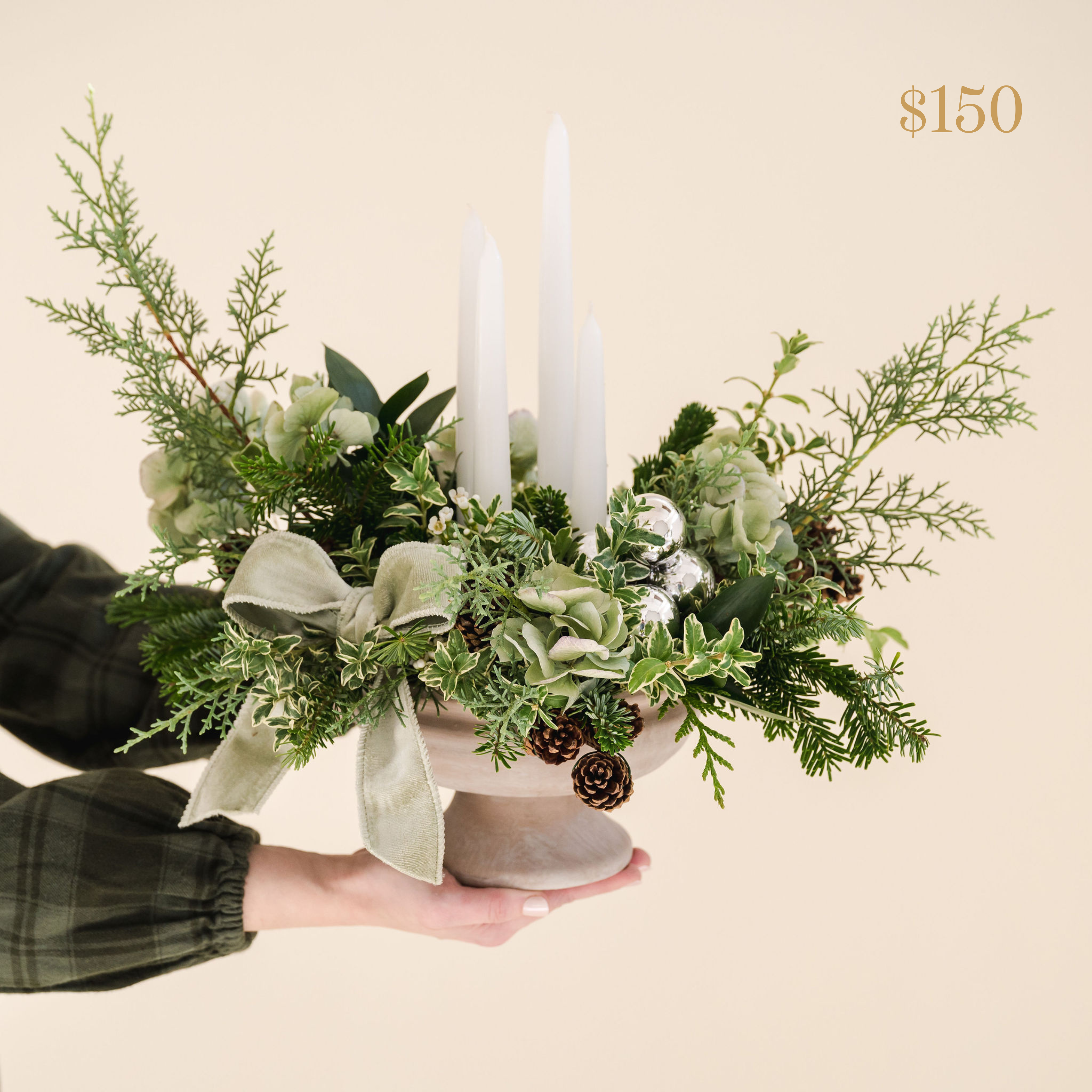 natural compote filled with fragrant greenery, taper candles, bow, shiny silver ball ornaments and natural pinecones. Text reading $150 value