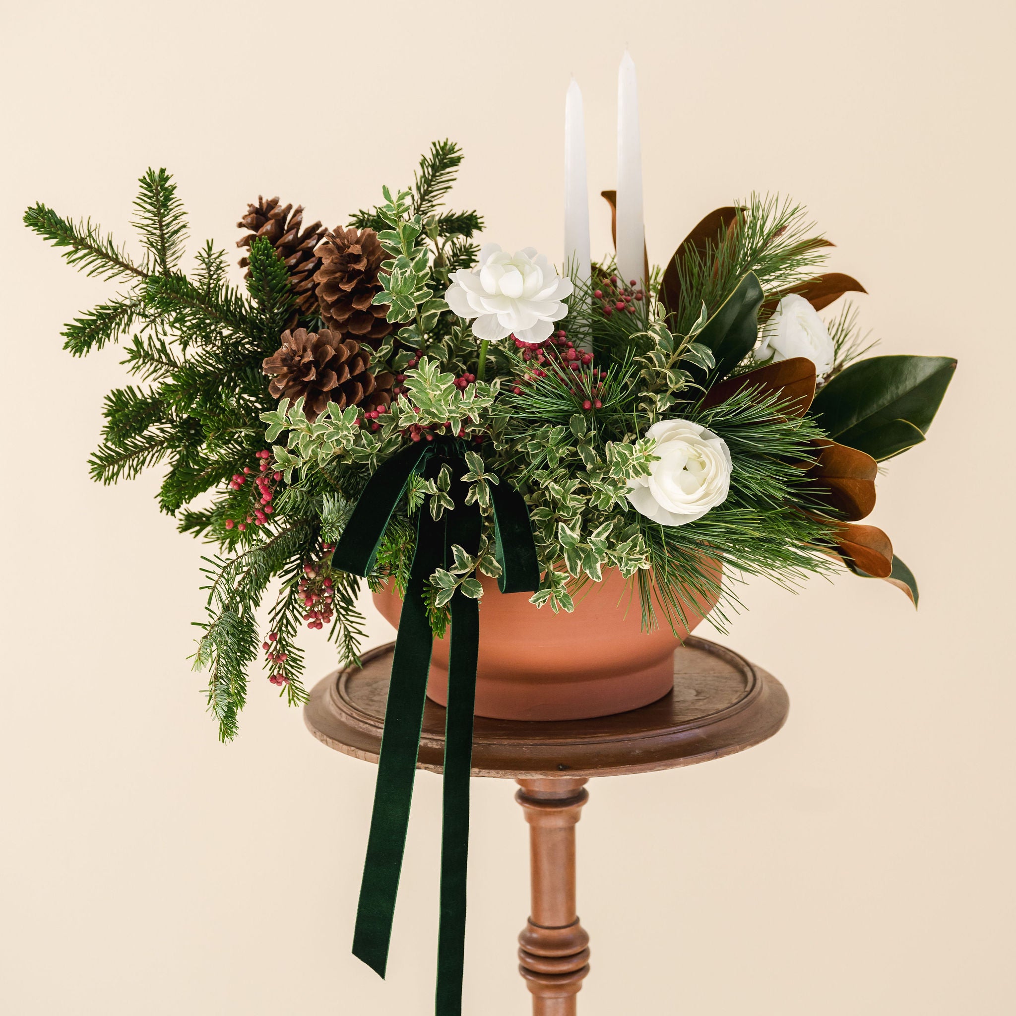 lush, fragrant greens, white ranunculus, 2 white taper candles, natural pinecones and a velvet box designed in a low terracotta vessel. 