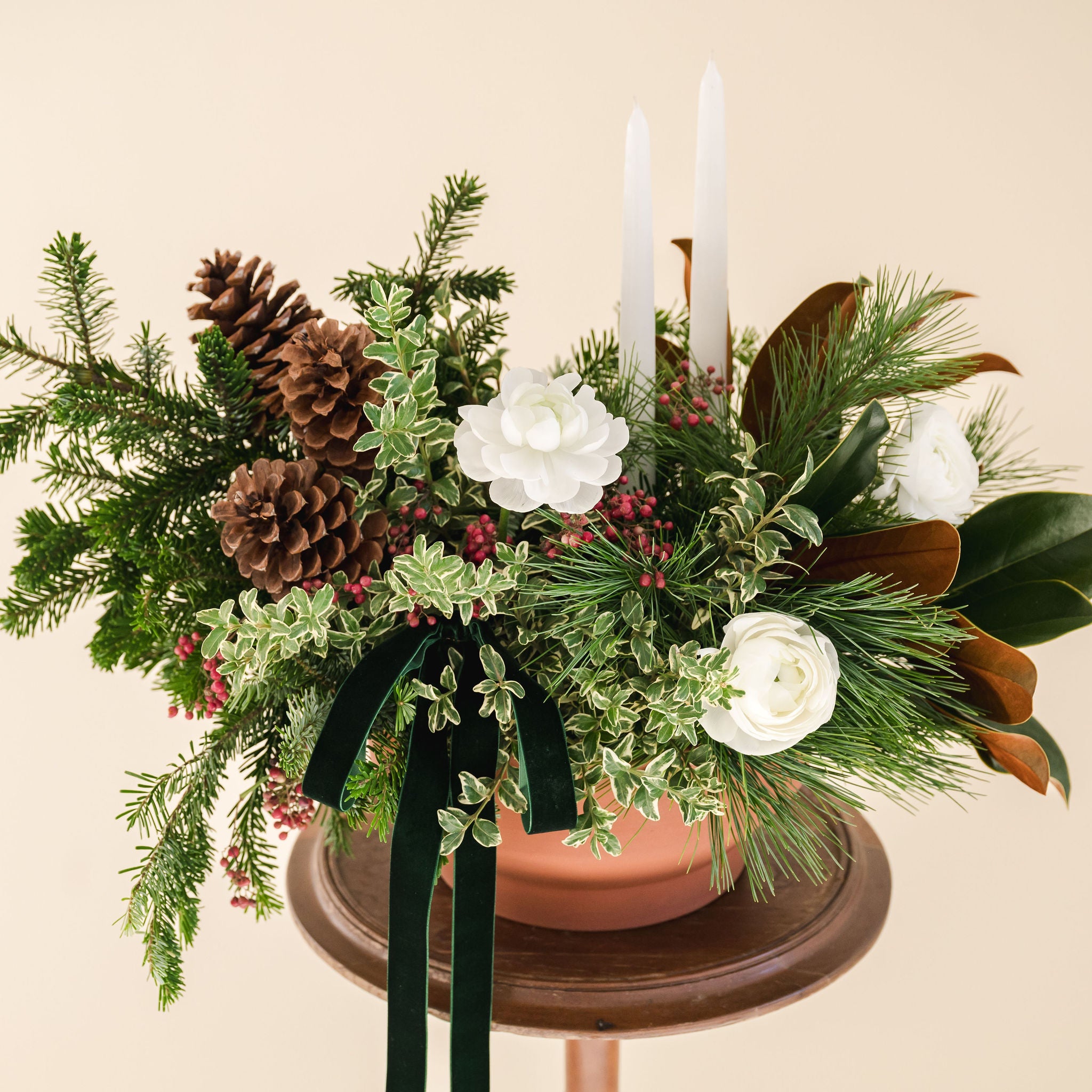 lush, fragrant greens, white ranunculus, 2 white taper candles, natural pinecones and a velvet box designed in a low terracotta vessel. 