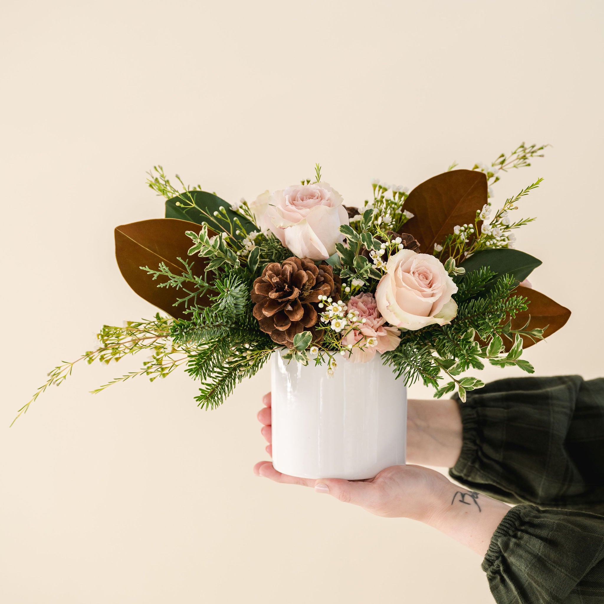 a white ceramic pot with fragrant winter greenery, natural pinecones and beautiful pink, taupe flowers