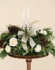 low arrangement of fragrant winter greens with white flowers, two white candles, natural pinecones and sage ribbon. 