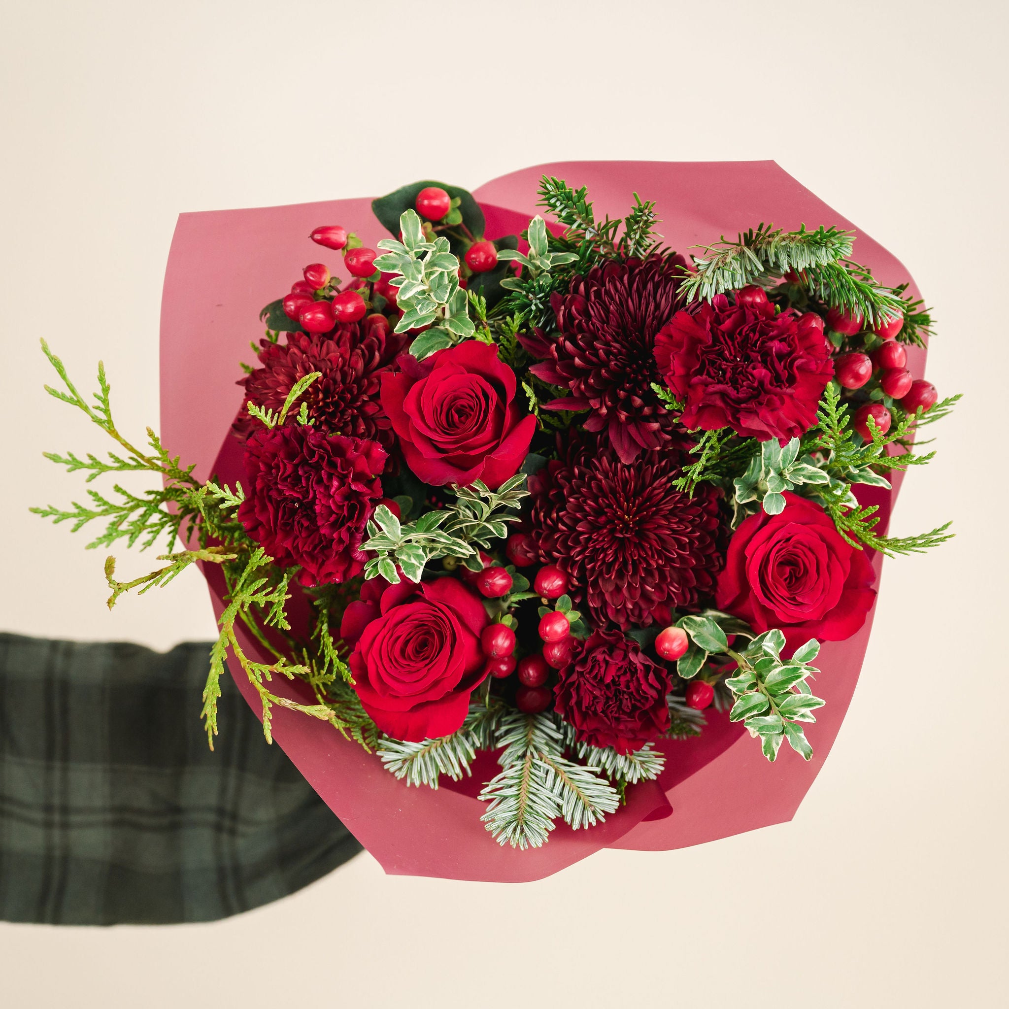 a bouquet of red and burgundy flowers with a mix of fragrant winter greenery