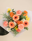 a bouquet of peach, orange, yellow and white flowers with a mix of greenery. 