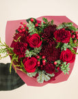 a bouquet of red and burgundy flowers with a mix of fragrant winter greenery