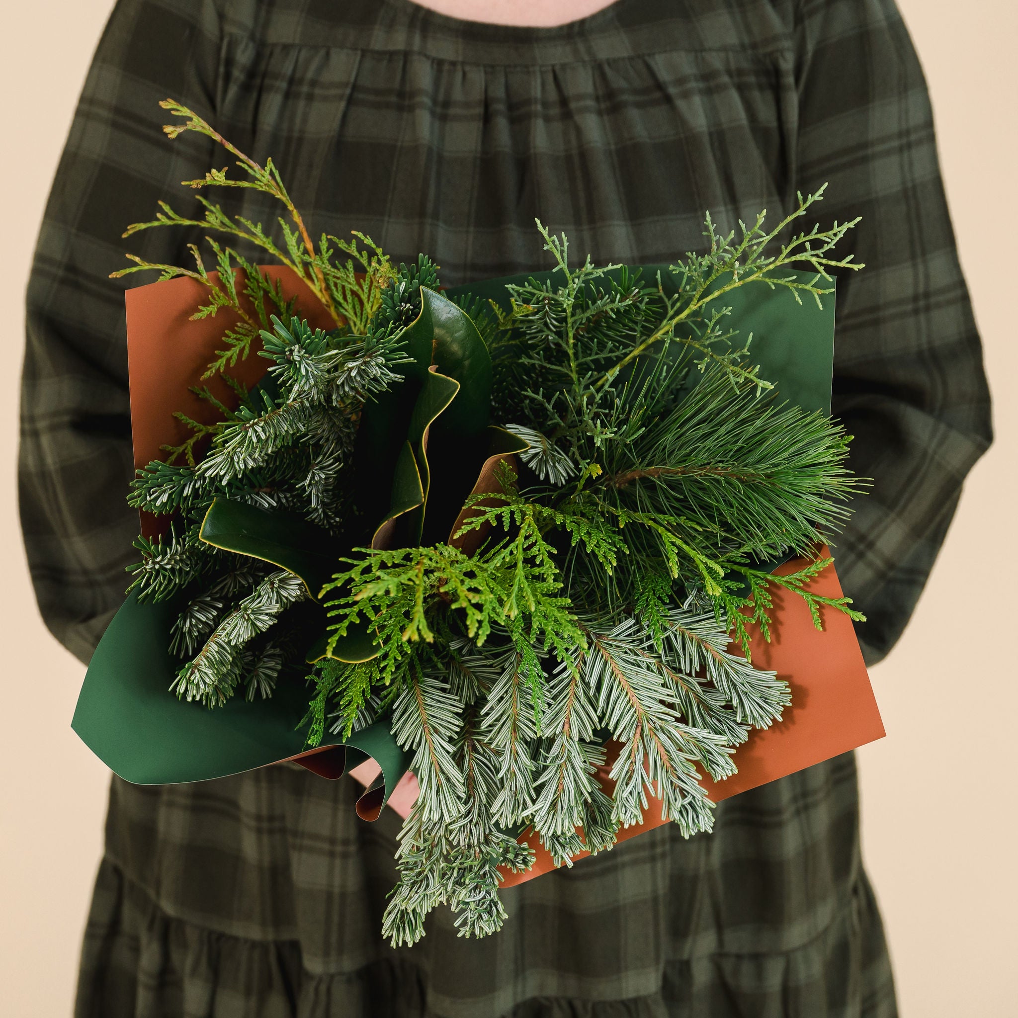 bouquet of mixed winter greenery, held by a person in a green dress