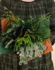 bouquet of mixed winter greenery, held by a person in a green dress