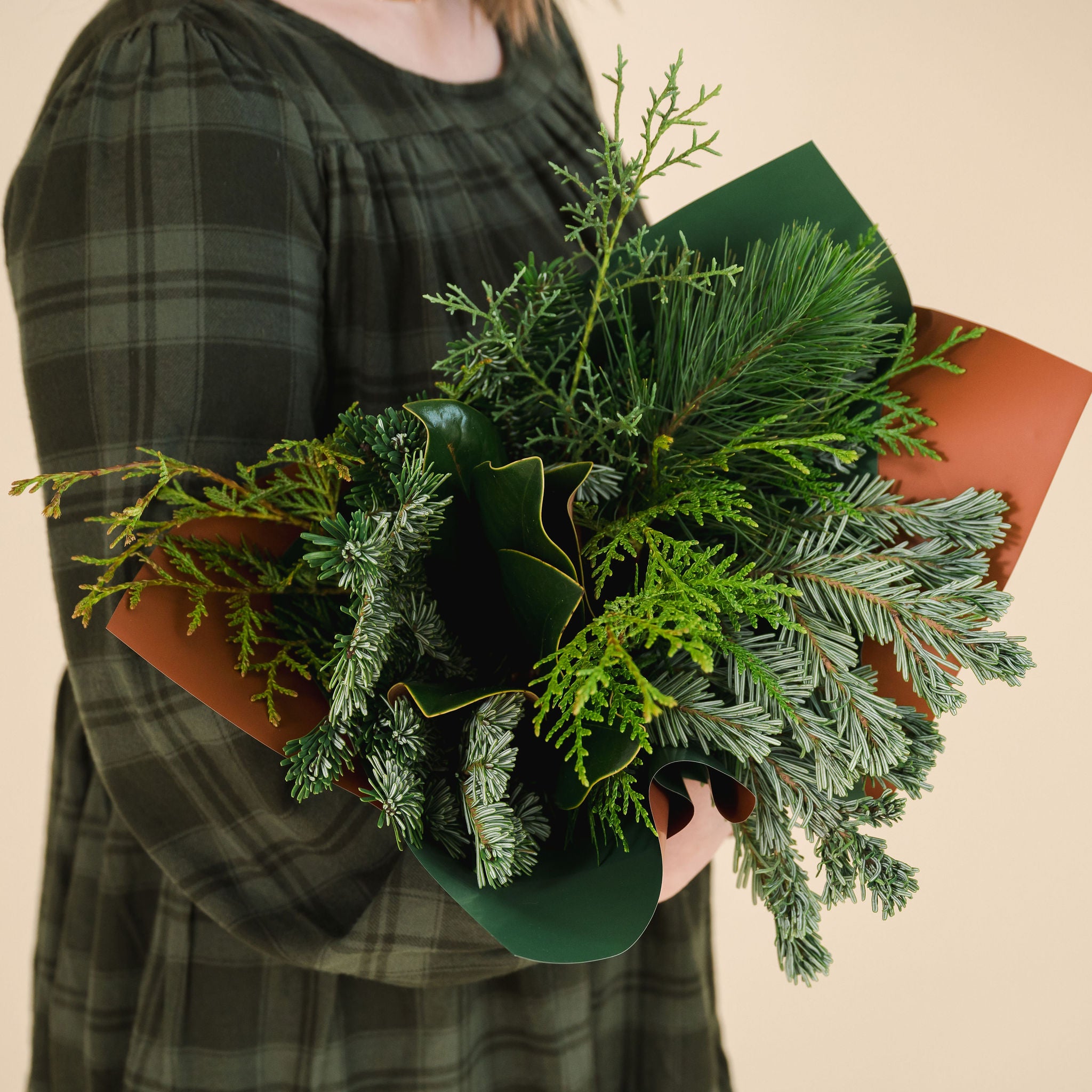 a variety of winter greens wrapped as a bouquet, held by a person in a green dress