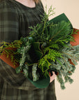 a variety of winter greens wrapped as a bouquet, held by a person in a green dress