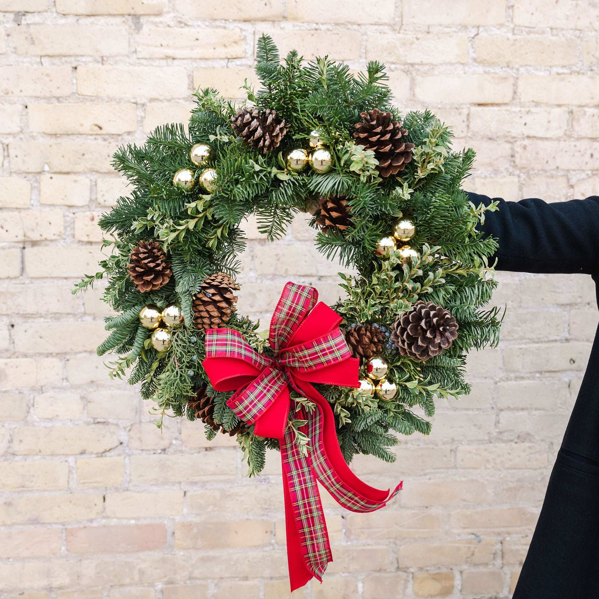 a wreath of fragrant winter greens, natural pinecones, shiny gold ball ornaments with a red and tartan bow