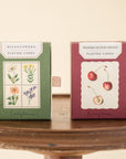 Wildflower and watercolour fruit playi8ng card boxes sitting on wooden sttol