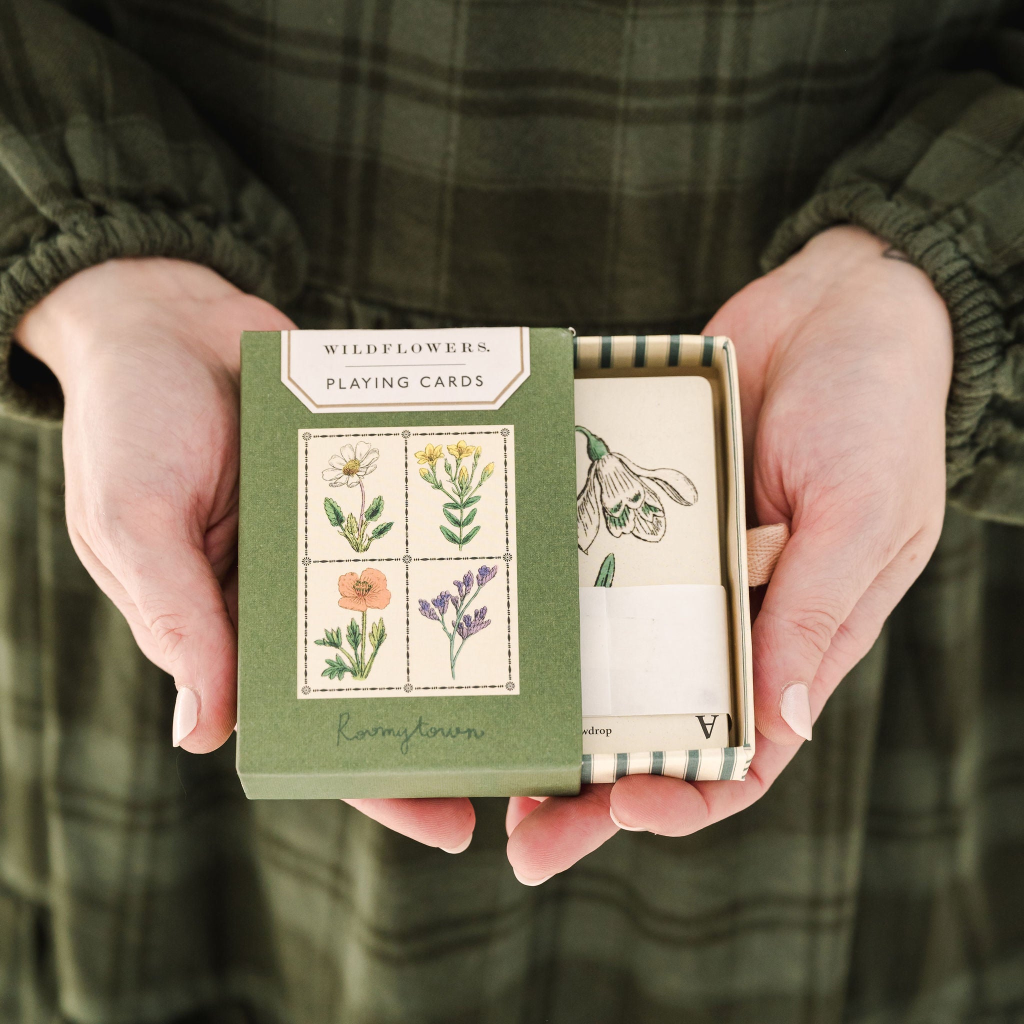 person in green dress holding wildflower playing card box