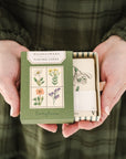 person in green dress holding wildflower playing card box