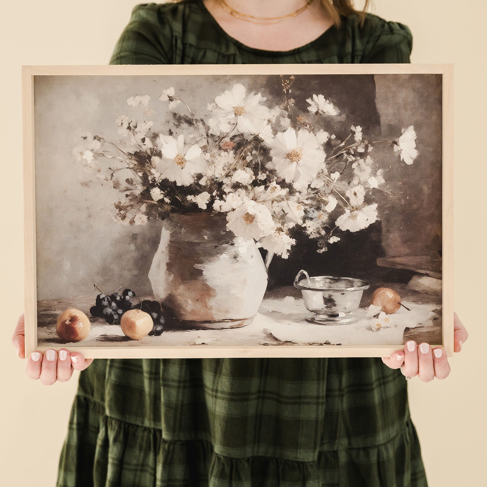 person in green dressing holding framed print of a vessel of white cosmos  and fruit