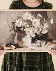 person in green dressing holding framed print of a vessel of white cosmos  and fruit