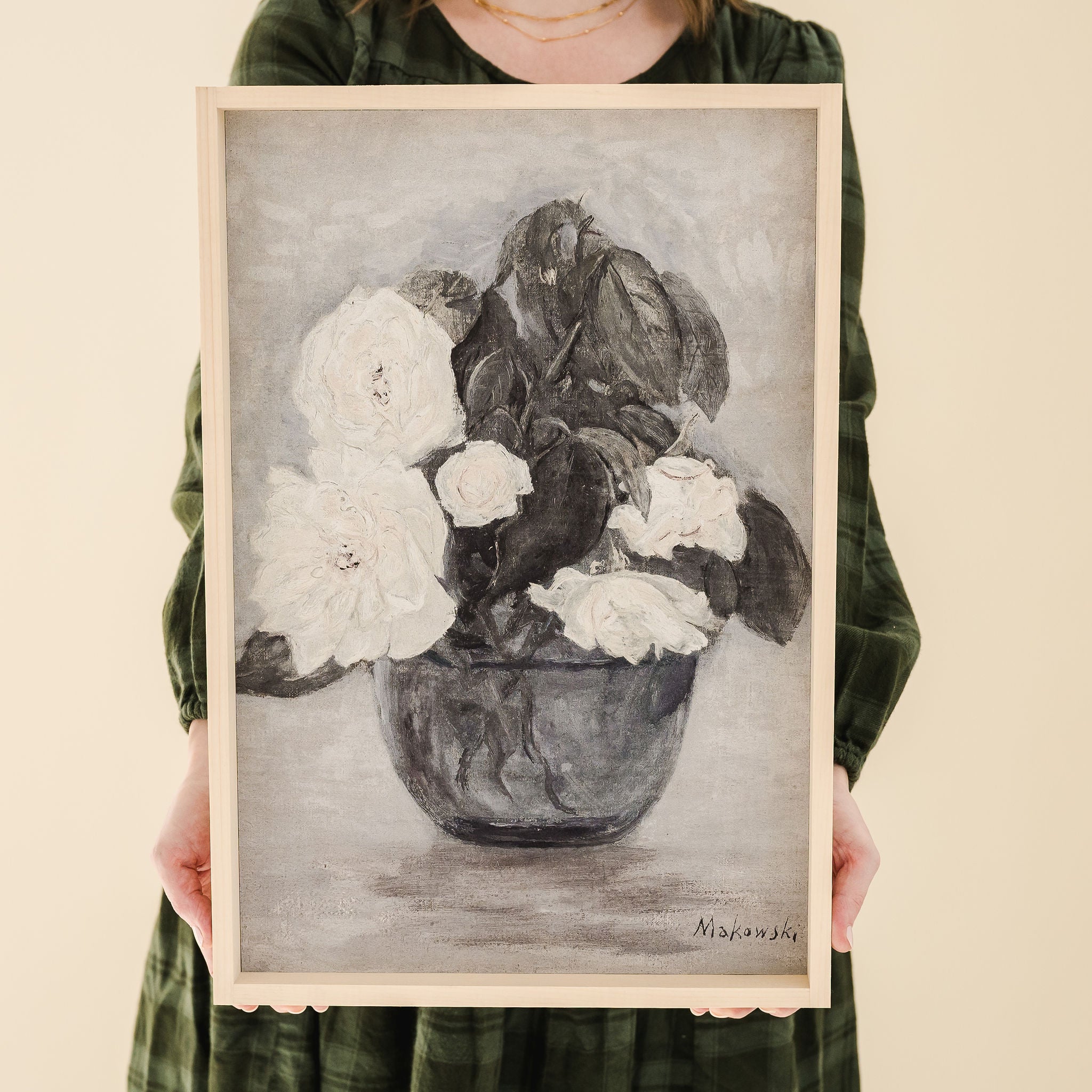 person in green dress holding framed print of white roses in a vase