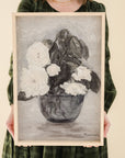 person in green dress holding framed print of white roses in a vase