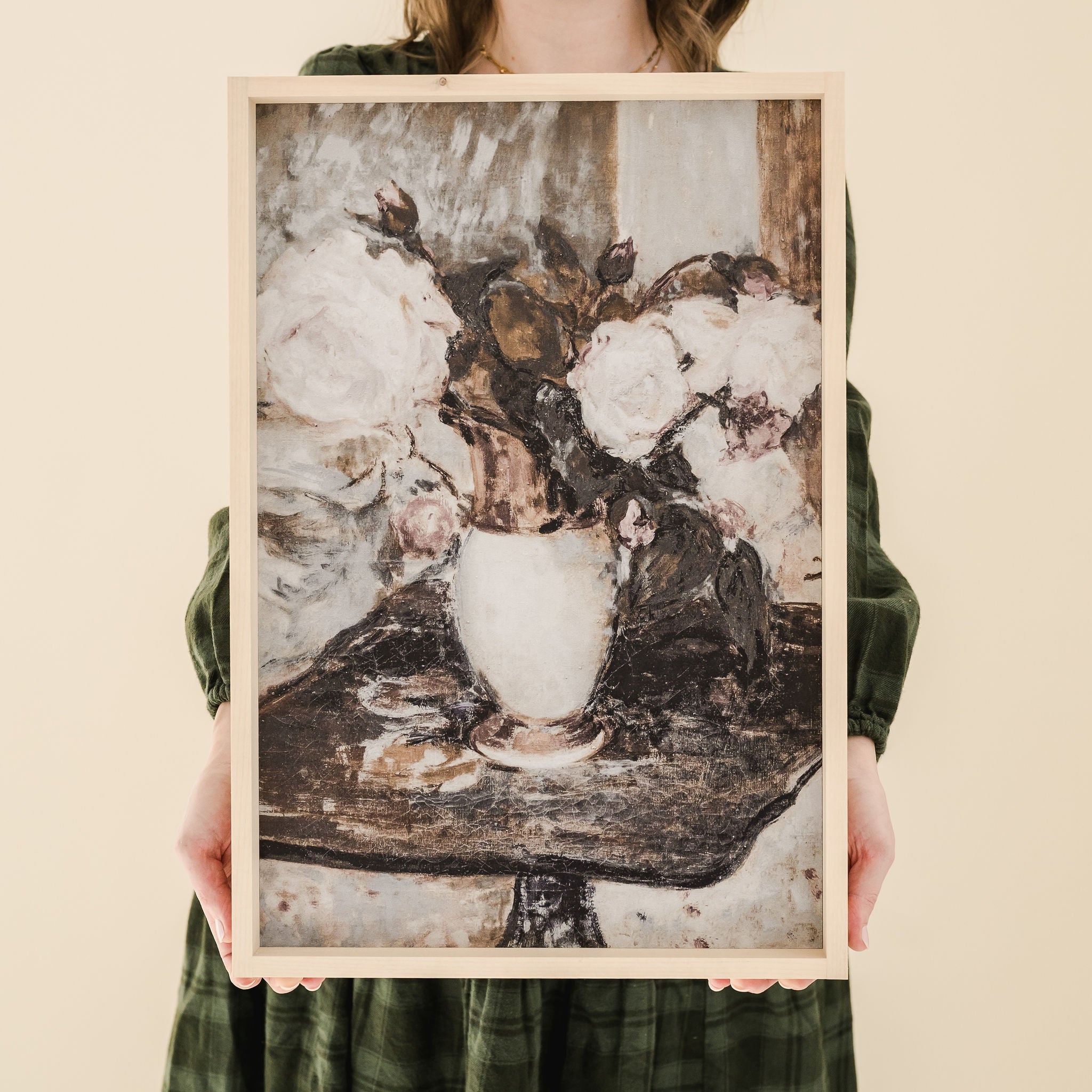 person in green dress holding framed print of white peonies in a vase