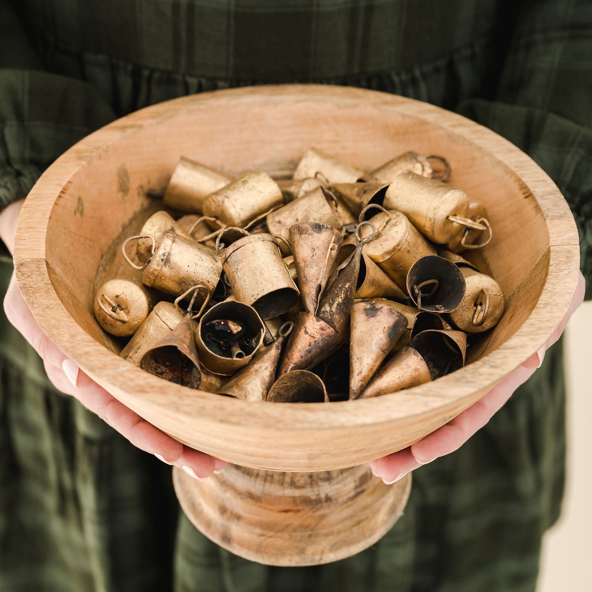 round wooden bowl filled with small gold bells help by someone in a green dress