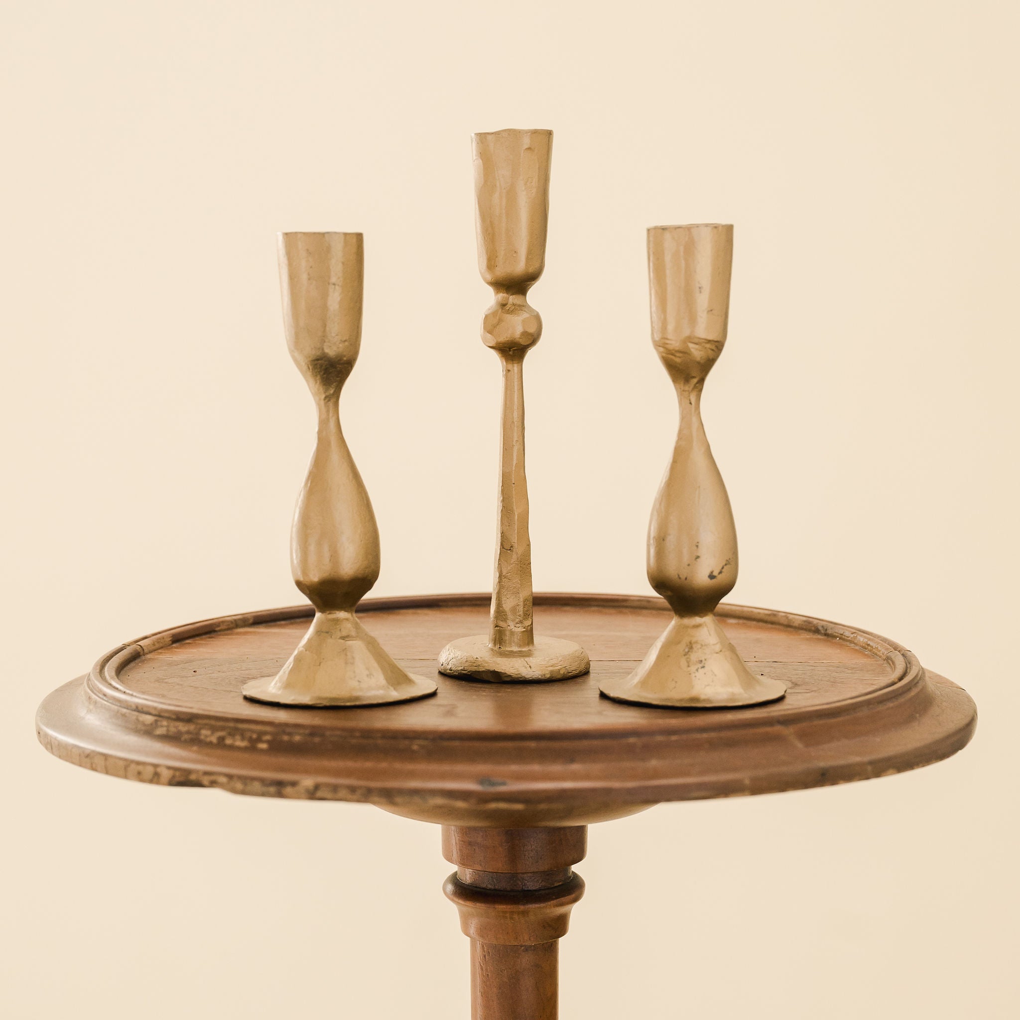 one tall and two short brass candlesticks on a wooden stool