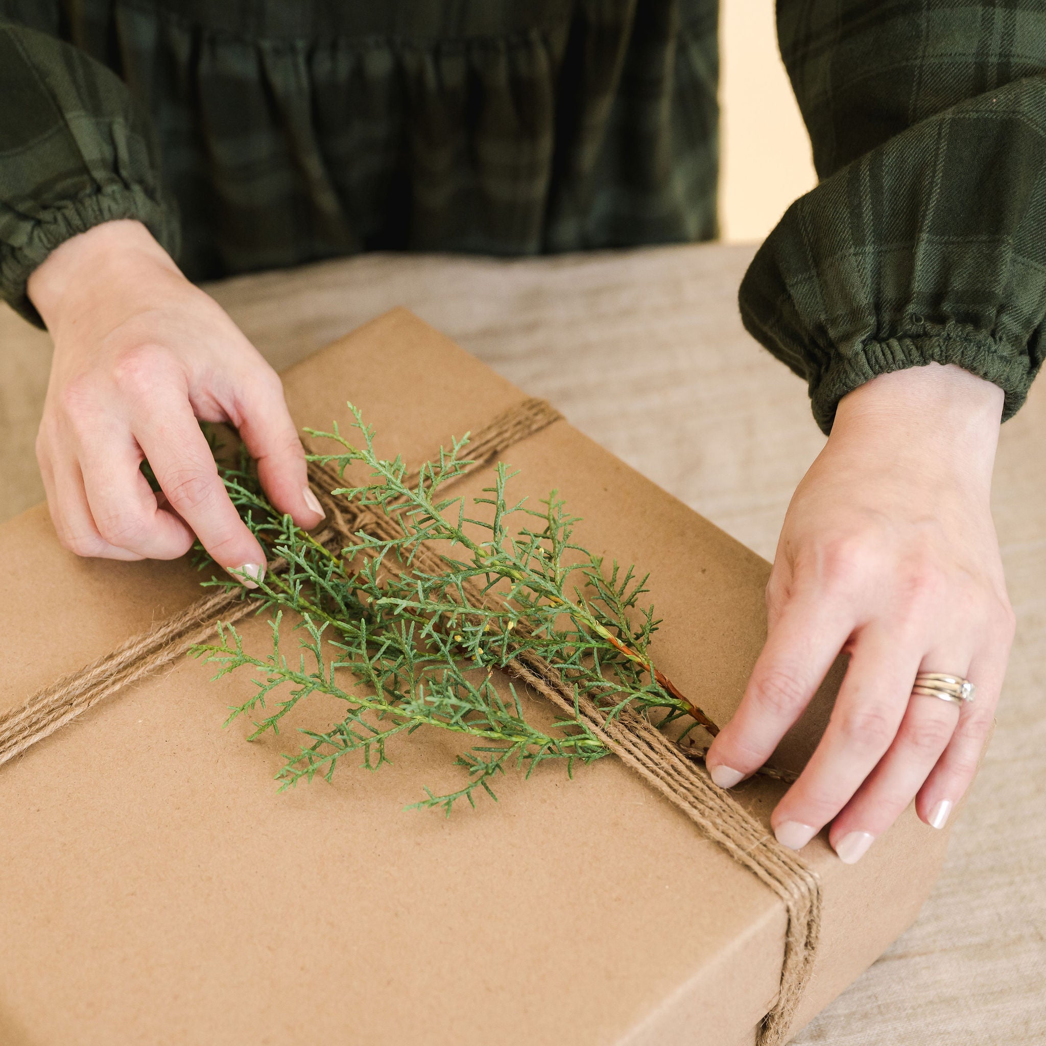 hands wrapping a gift with winter greenery on top