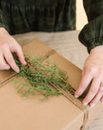 hands wrapping a gift with winter greenery on top