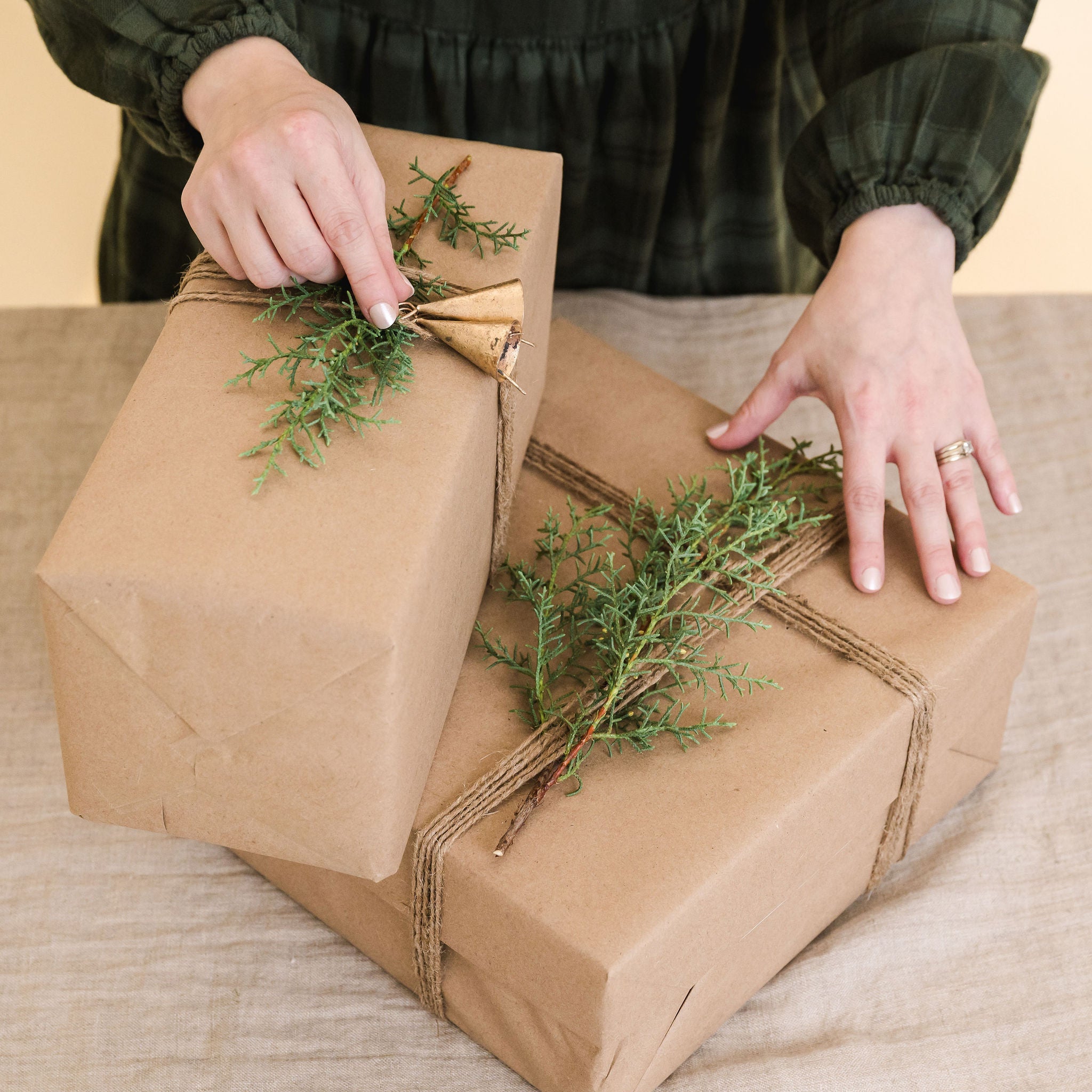 two wrapped gifts with a piece of greenery on top and two gold bells