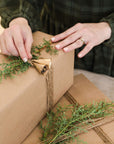 wrapped gift with winter greenery and two gold bells on top