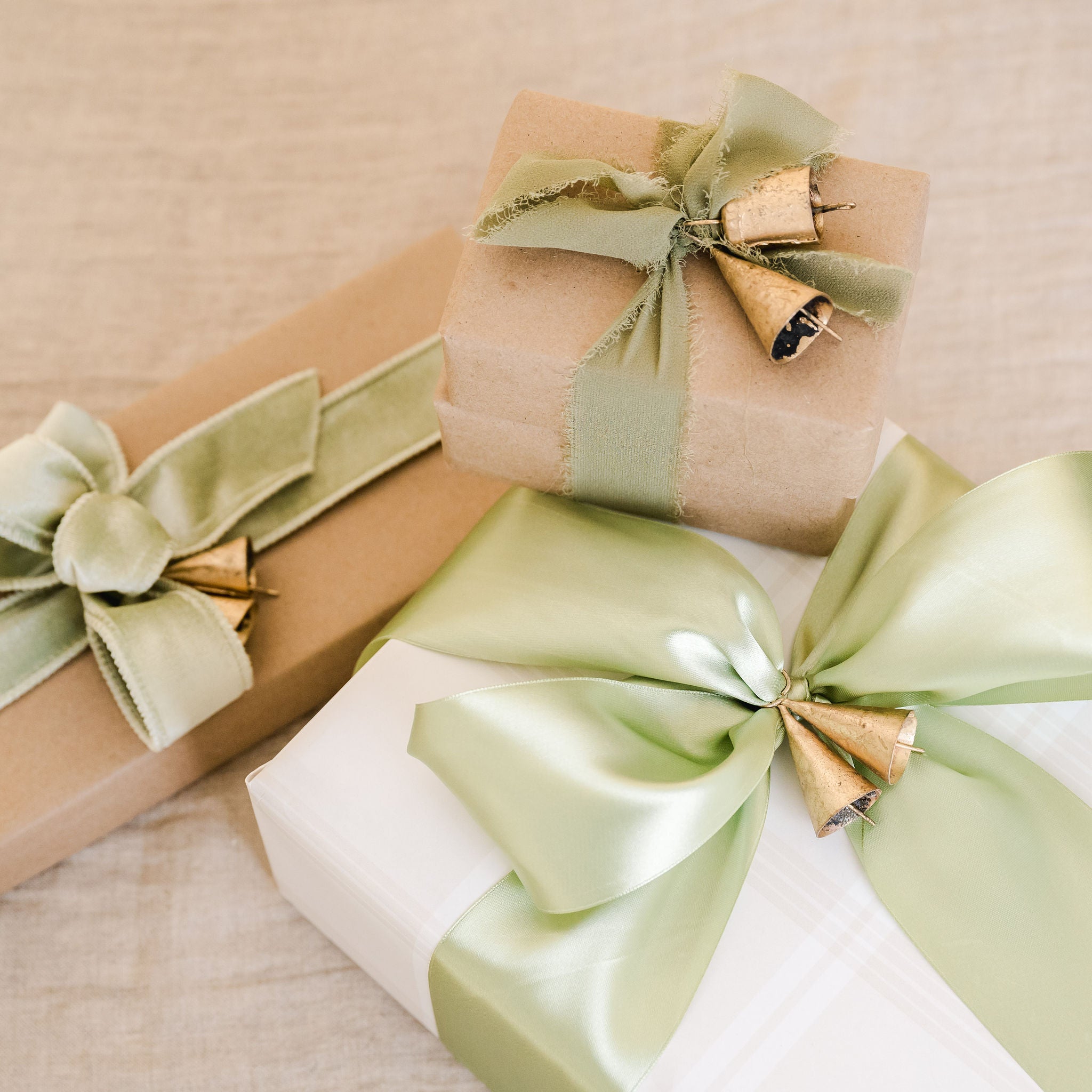 three gifts wrapped with sage ribbon and gold bells