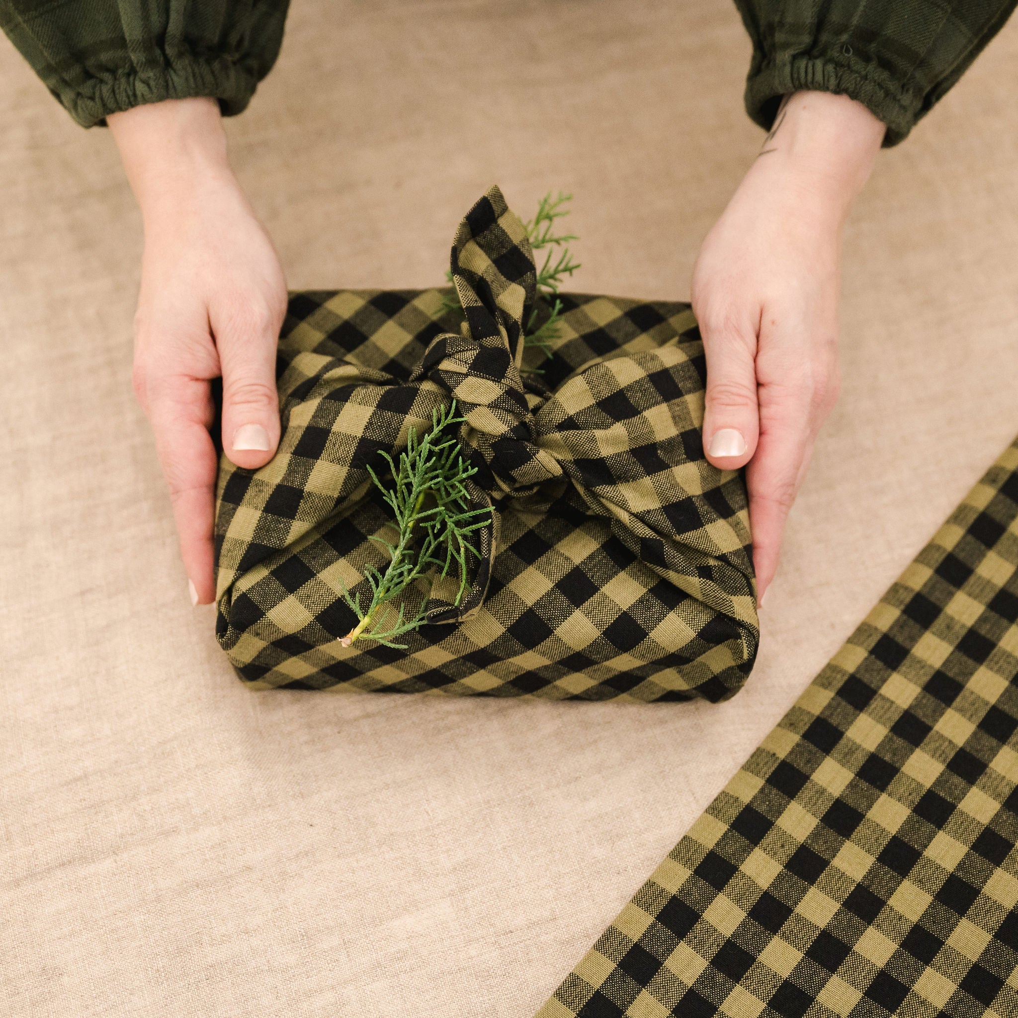 green and black gingham tea towel used as gift wrap topped with a piece of greenery