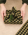 green and black gingham tea towel used as gift wrap topped with a piece of greenery