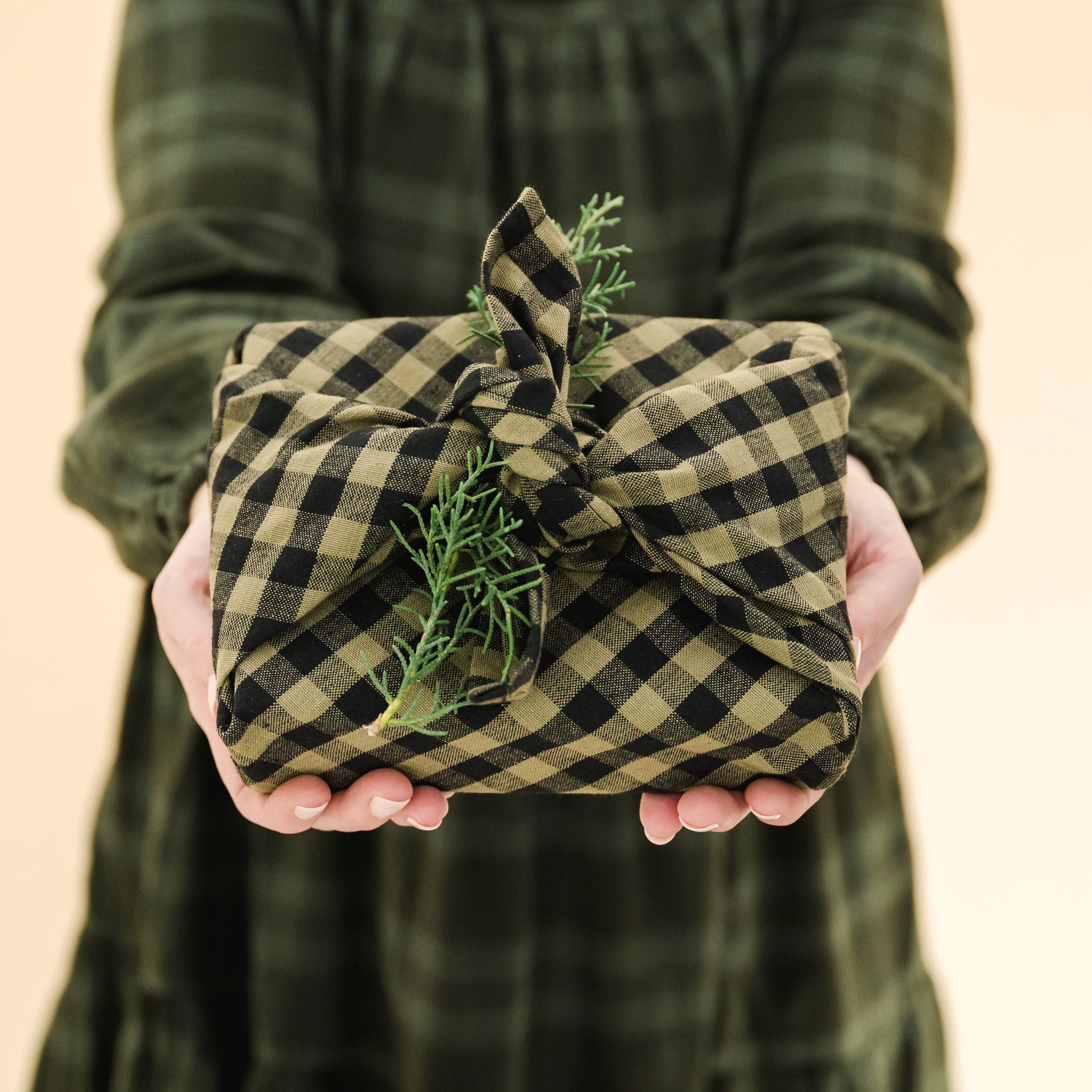 green and black gingham tea towel used as gift wrap topped with a piece of greenery