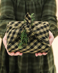 green and black gingham tea towel used as gift wrap topped with a piece of greenery