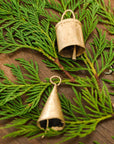 two gold bells laying on a stem of cedar