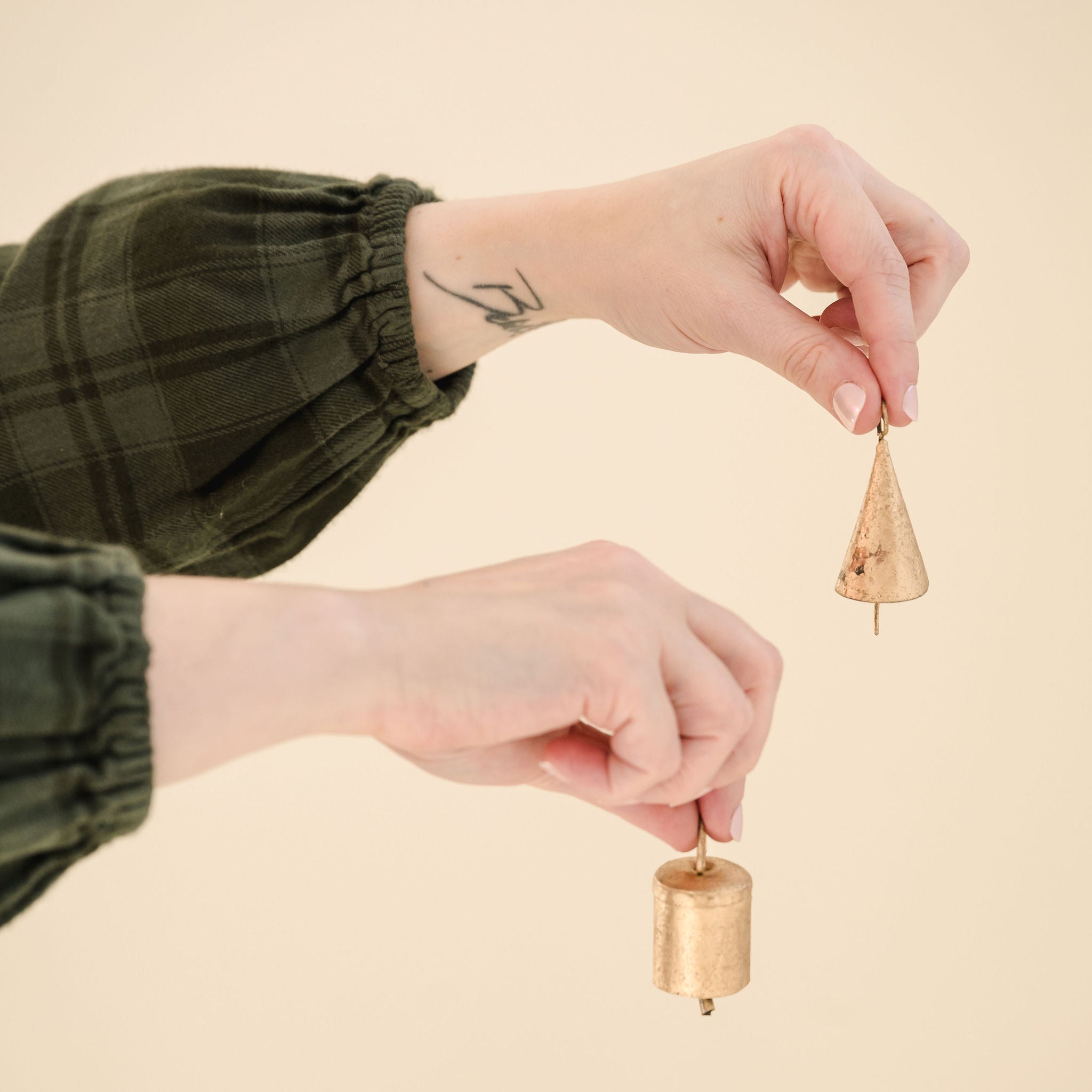 two hands holding small gold bells